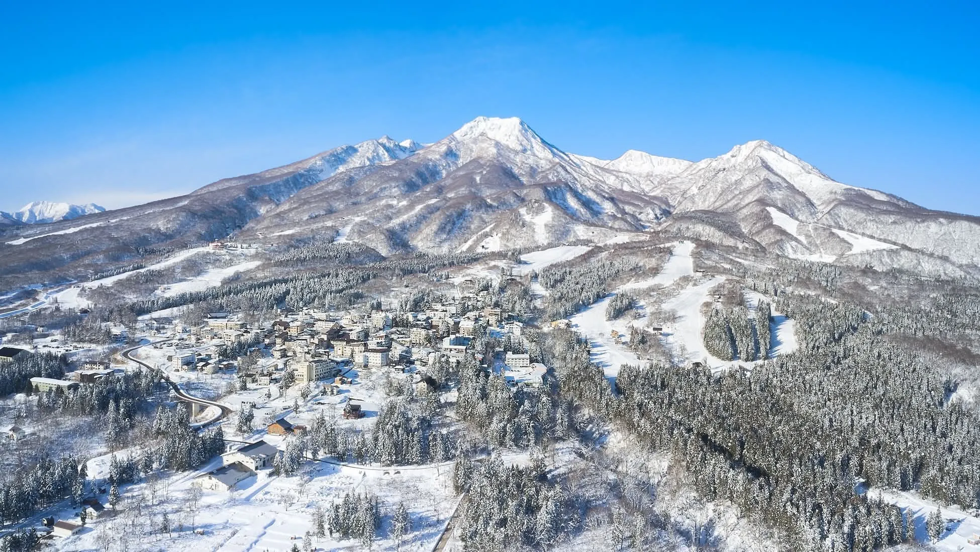 Elevated view of Akakura Onsen village nestled below snow-covered ski slopes and forested mountains