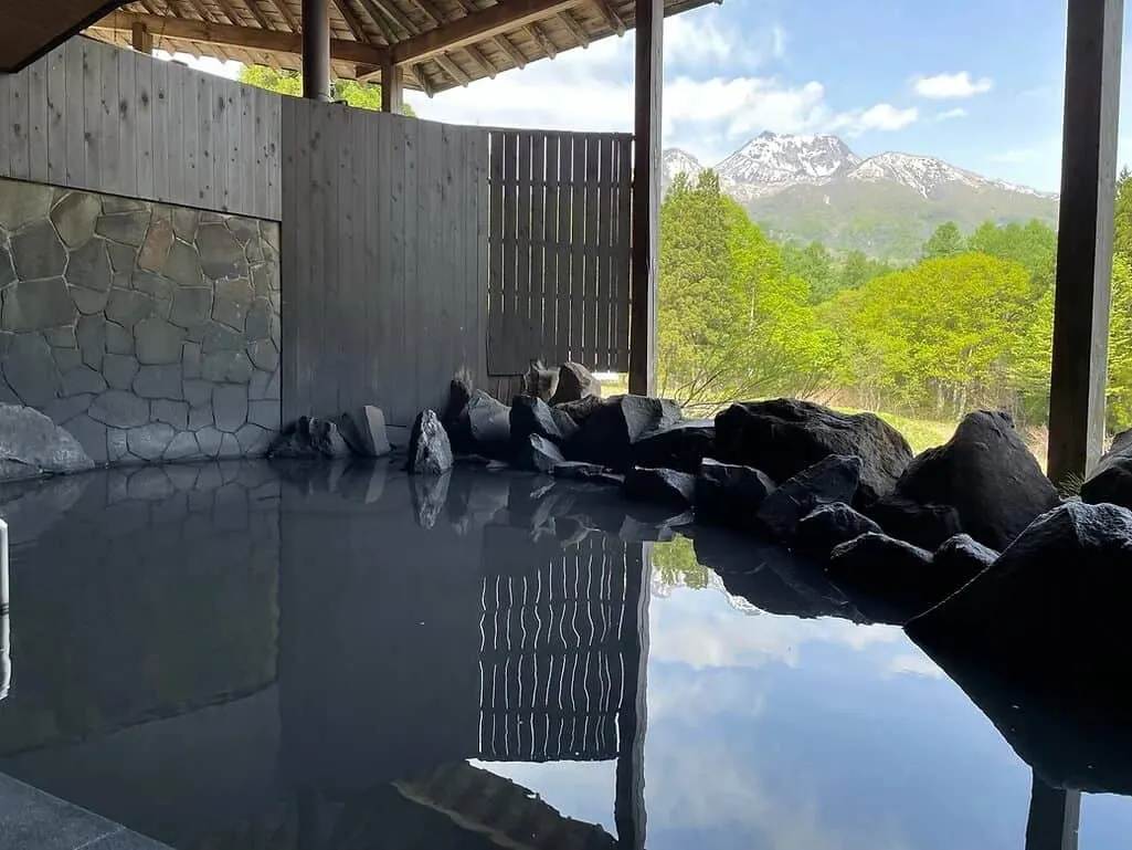 Outdoor hot spring rotenburo with natural stone bath framing views of Mount Myoko and snowy trees